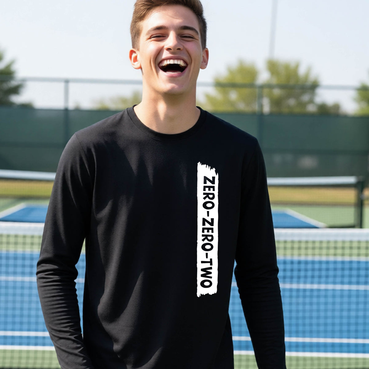 A close-up of a young person on a pickleball wearing a black short-sleeve t-shirt, , with a white graphic of artistic banner with the cutout words of ‘ZERO ZERO TWO’ , on the front of the shirt. 
