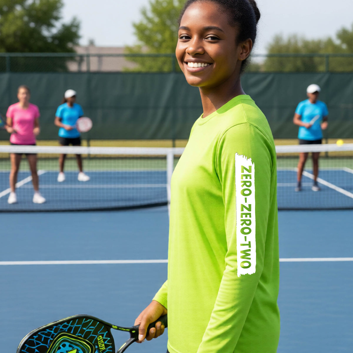 A close-up of a young person on a pickleball wearing a lime green short-sleeve t-shirt, , with a white graphic of artistic banner with the cutout words of ‘ZERO ZERO TWO’ , on the sleeve of the shirt. 