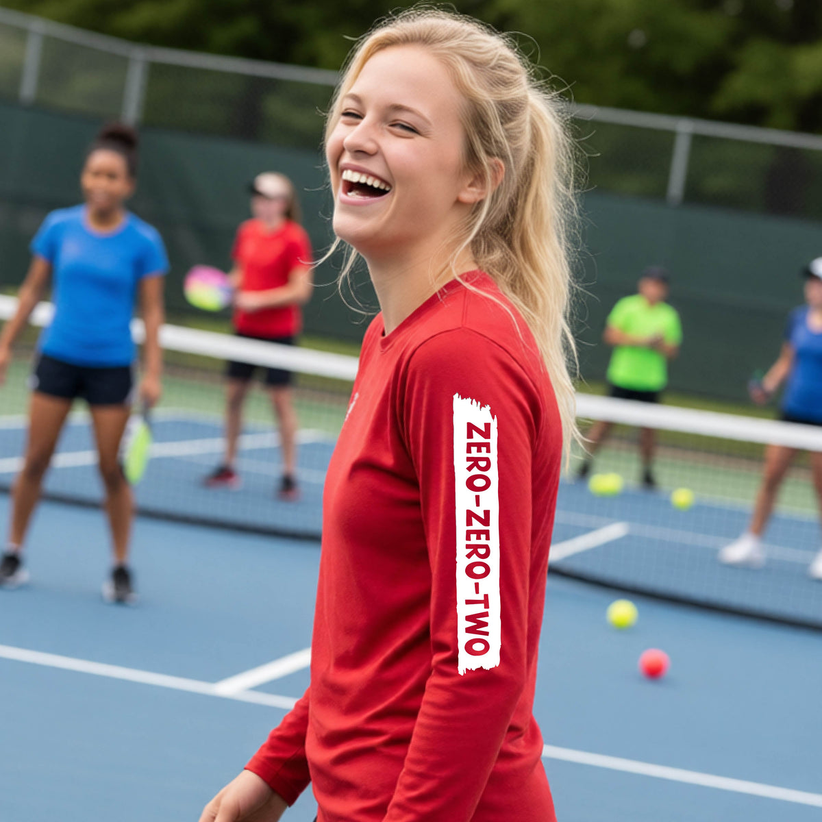 A close-up of a young person on a pickleball wearing a red short-sleeve t-shirt, , with a white graphic of artistic banner with the cutout words of ‘ZERO ZERO TWO’ , on the sleeve of the shirt. 