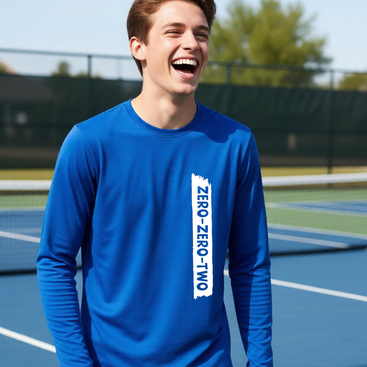 A close-up of a young person on a pickleball wearing a royal blue short-sleeve t-shirt, , with a white graphic of artistic banner with the cutout words of ‘ZERO ZERO TWO’ , on the front of the shirt. 