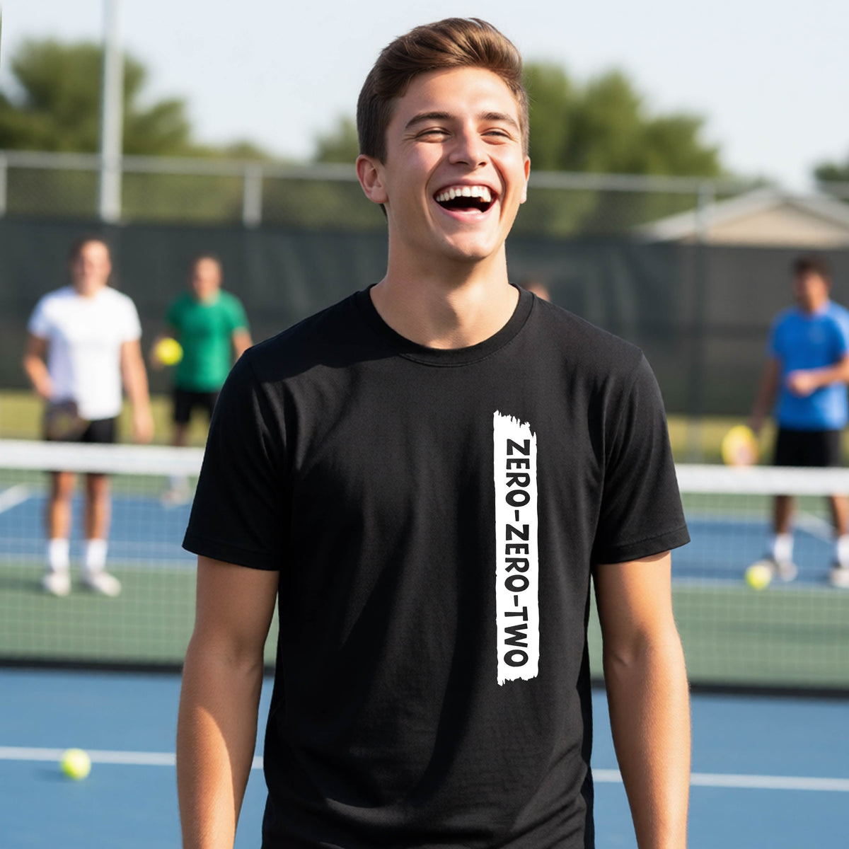 A close-up of a young person on a pickleball wearing a black short-sleeve t-shirt, , with a white graphic of artistic banner with the cutout words of ‘ZERO ZERO TWO’ , on the front of the shirt. 