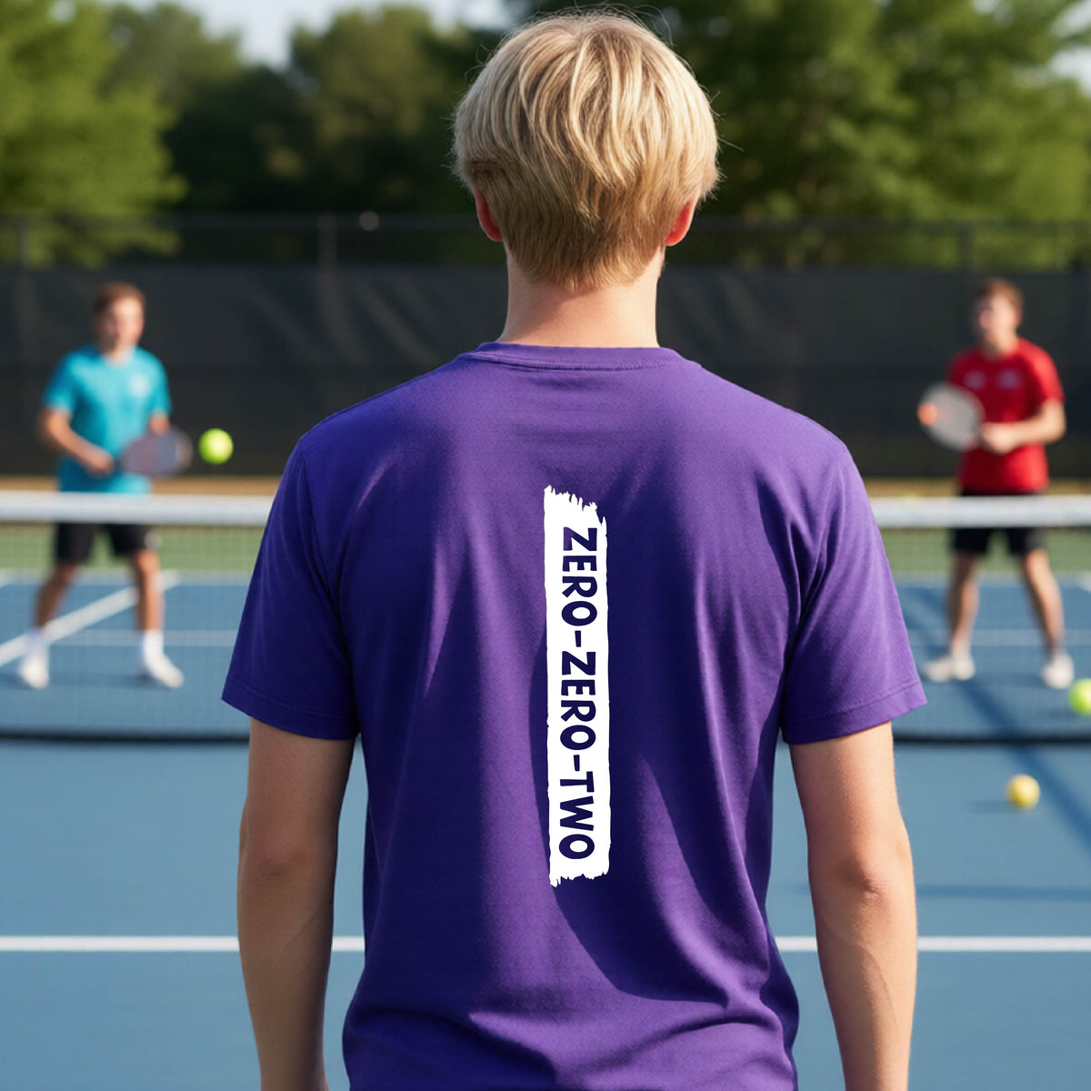A close-up of a young person on a pickleball wearing an purple short-sleeve t-shirt, , with a white graphic of artistic banner with the cutout words of ‘ZERO ZERO TWO’ , on the back of the shirt. 
