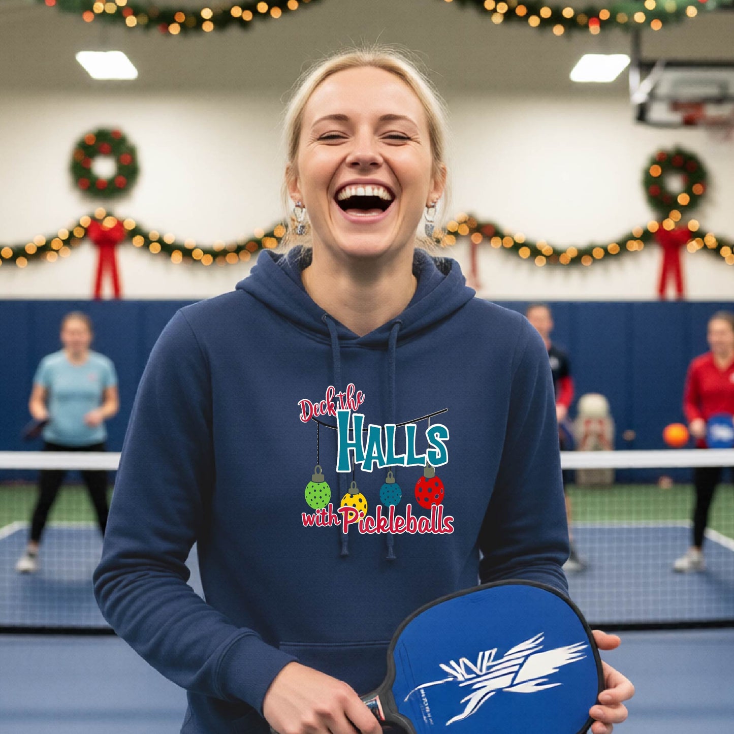 A navy blue hooded sweatshirt featuring a graphic print that reads "Deck the Halls with Picleballs" . The backgro0und is Christmas themed. 