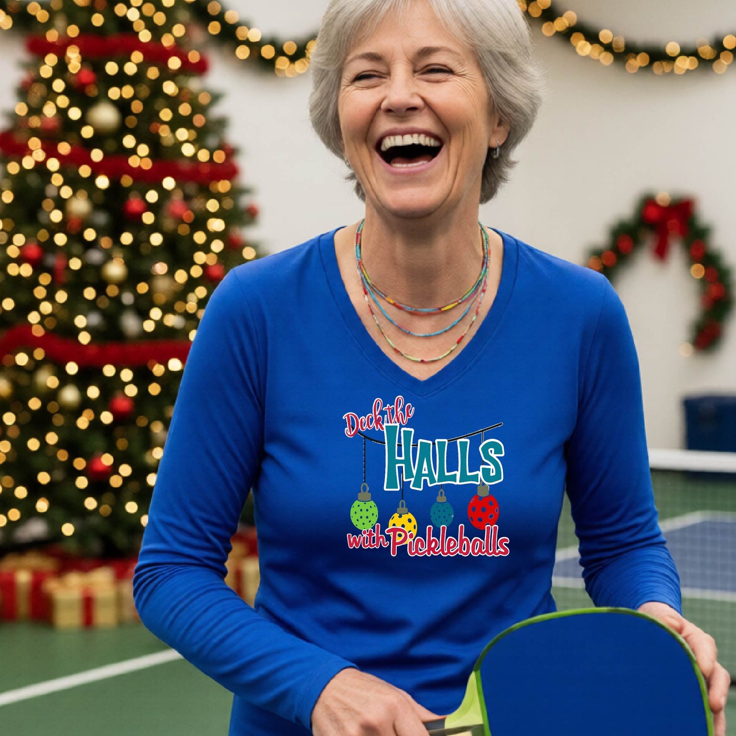 A women's royal blue long-sleeve v-neck shirt featuring a pickleball graphic with text "DECK THE HALLS WITH PICKLEBALLS"  and  Christmas themed background. 