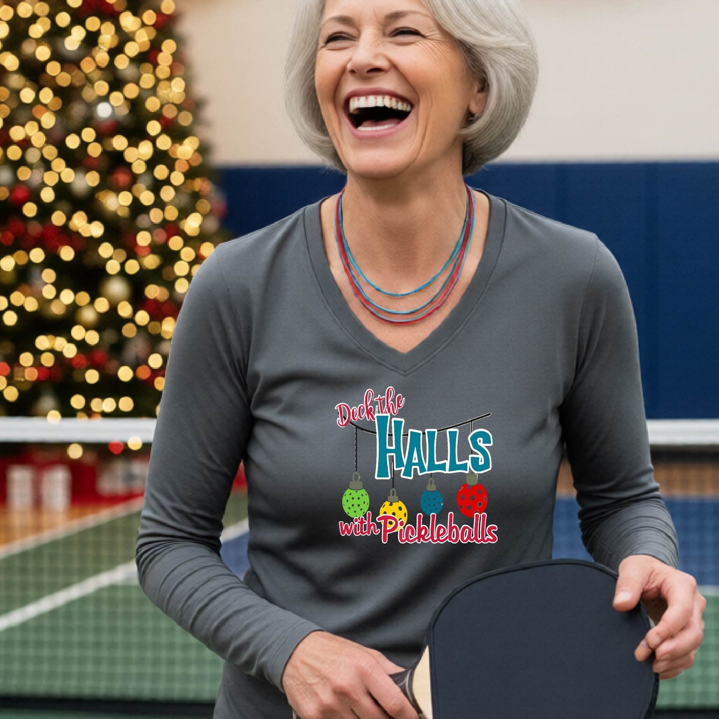 A women's gray long-sleeve v-neck shirt featuring a pickleball graphic with text "DECK THE HALLS WITH PICKLEBALLS"  and  Christmas themed background. 