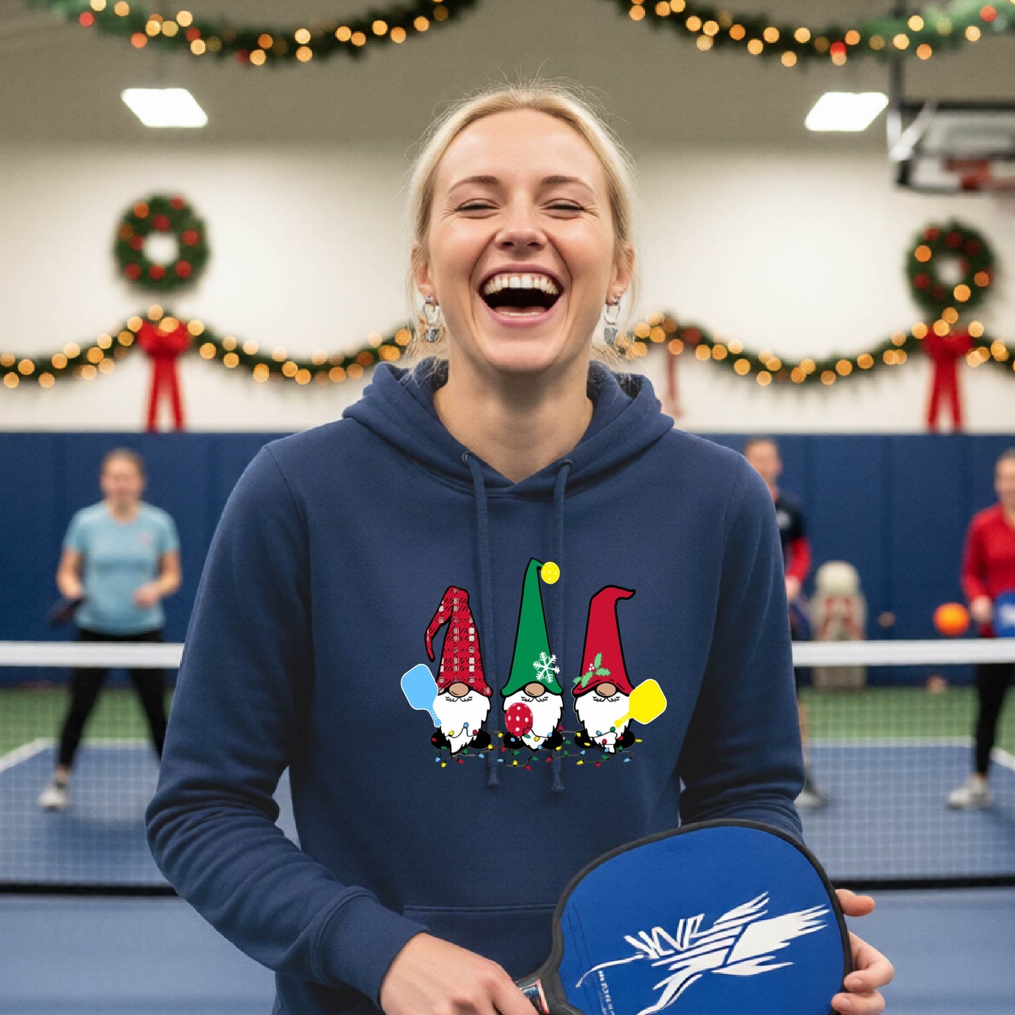 A navy blue  hooded sweatshirt featuring a pickleball graphic with gnomes wearing Chrsitmas hats and holding pickleball paddles and a Christmas themed bakground. 