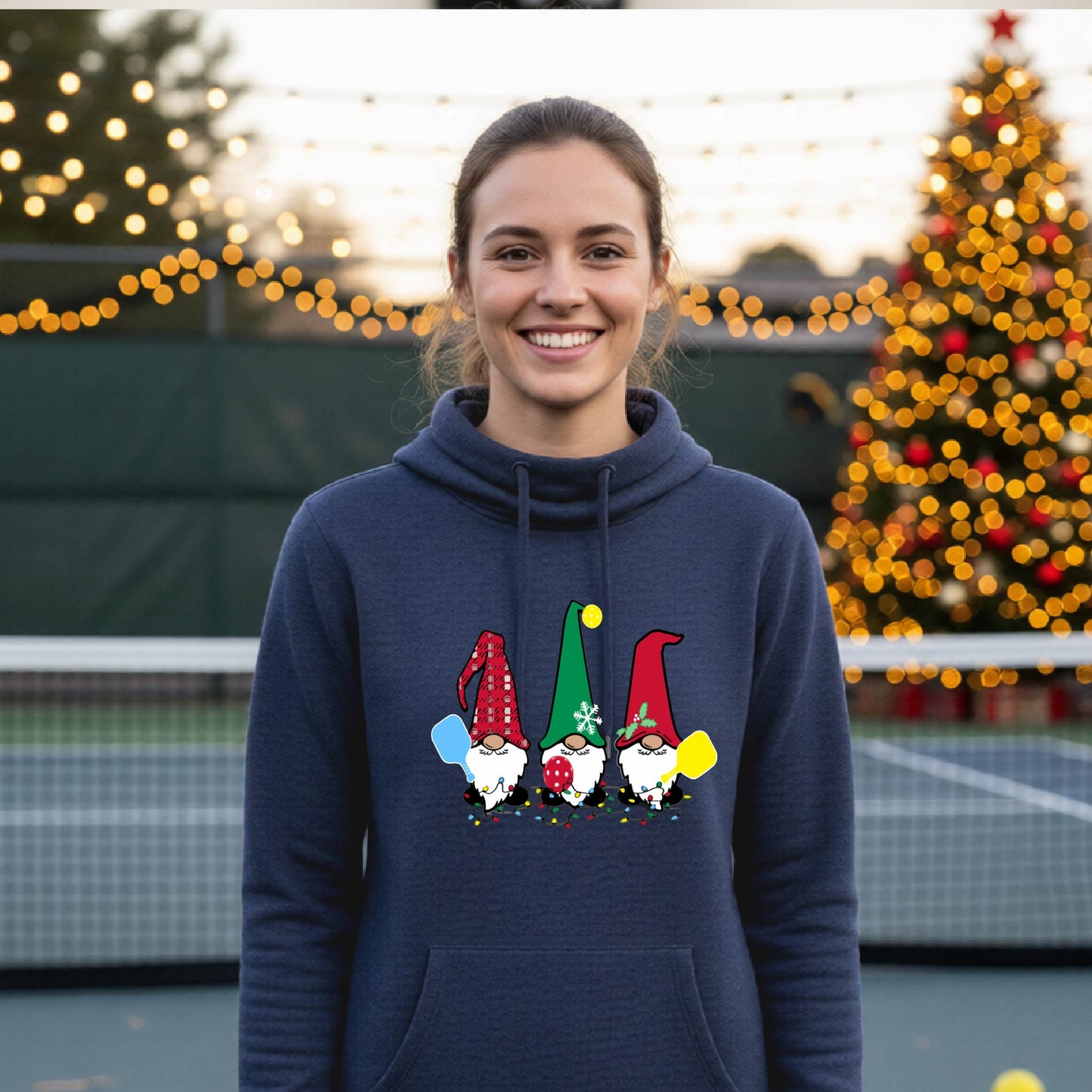 A navy blue cowl-neck  hooded sweatshirt featuring a pickleball graphic with gnomes wearing Christmas hats and holding pickleball paddles and a Christmas themed background. 