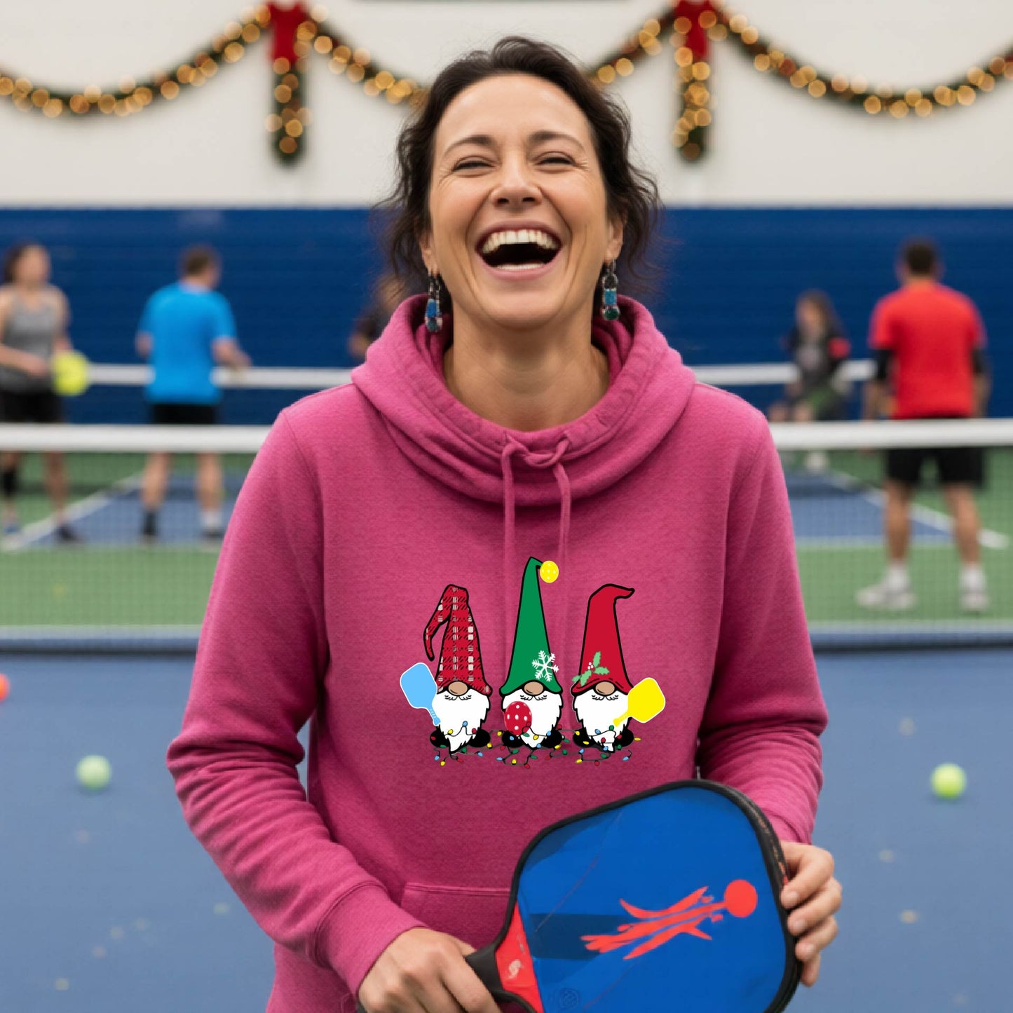 A pink cowl-neck  hooded sweatshirt featuring a pickleball graphic with gnomes wearing Christmas hats and holding pickleball paddles and a Christmas themed background. 