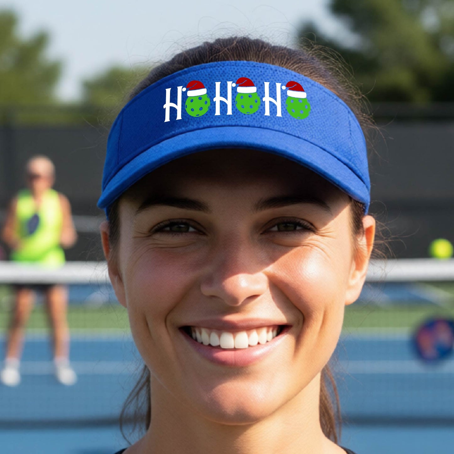 A royal blue visor with a pickleball Christmas graphic of the text "HO HO HO" with the O replaced by green picklebalsl paddle  santa hats. 