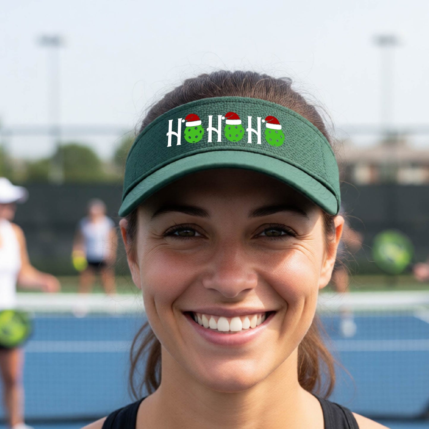 A green visor with a pickleball Christmas graphic of the text "HO HO HO" with the O replaced by green picklebalsl paddle  santa hats. 