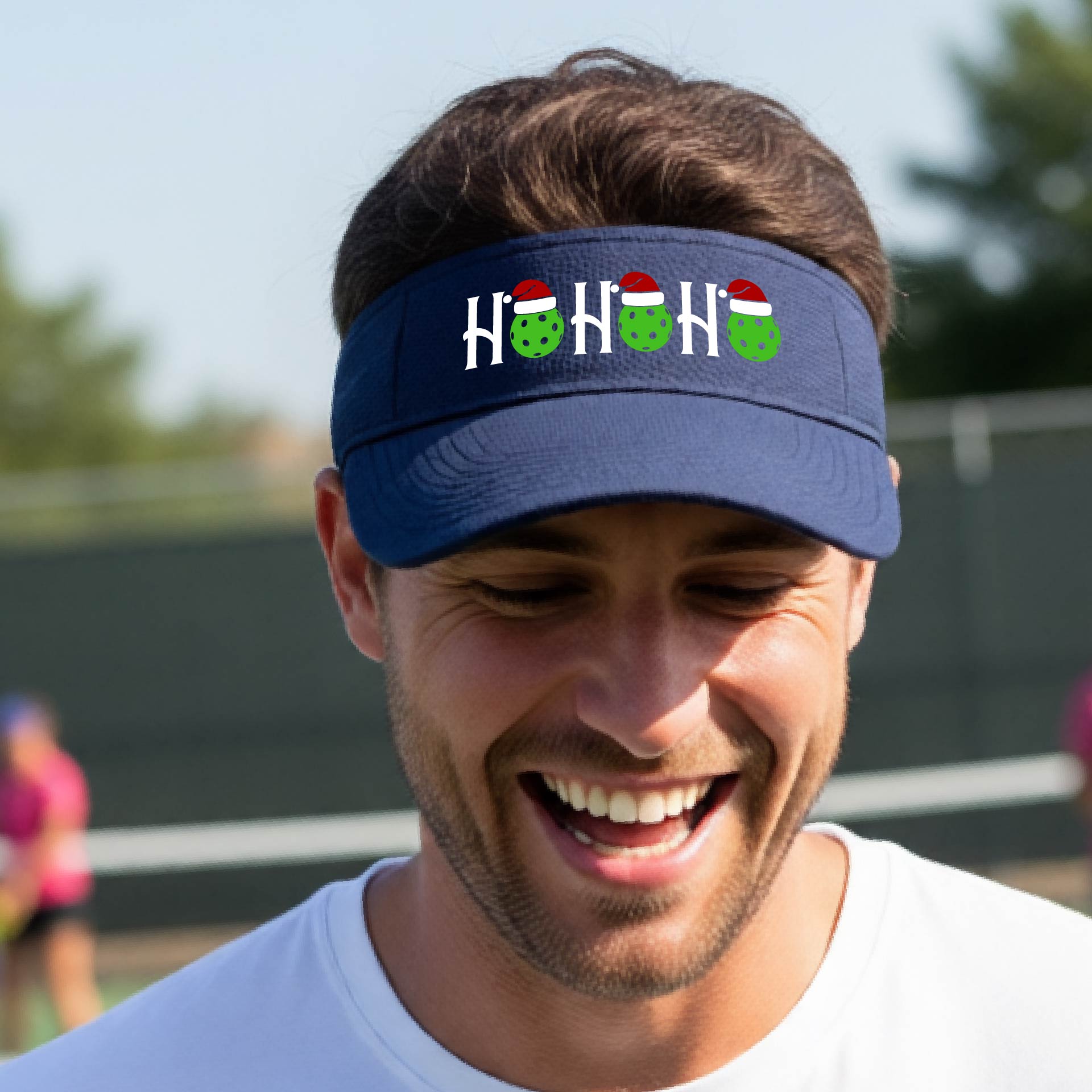 A navy blue visor with a pickleball Christmas graphic of the text "HO HO HO" with the O replaced by green picklebalsl paddle  santa hats. 