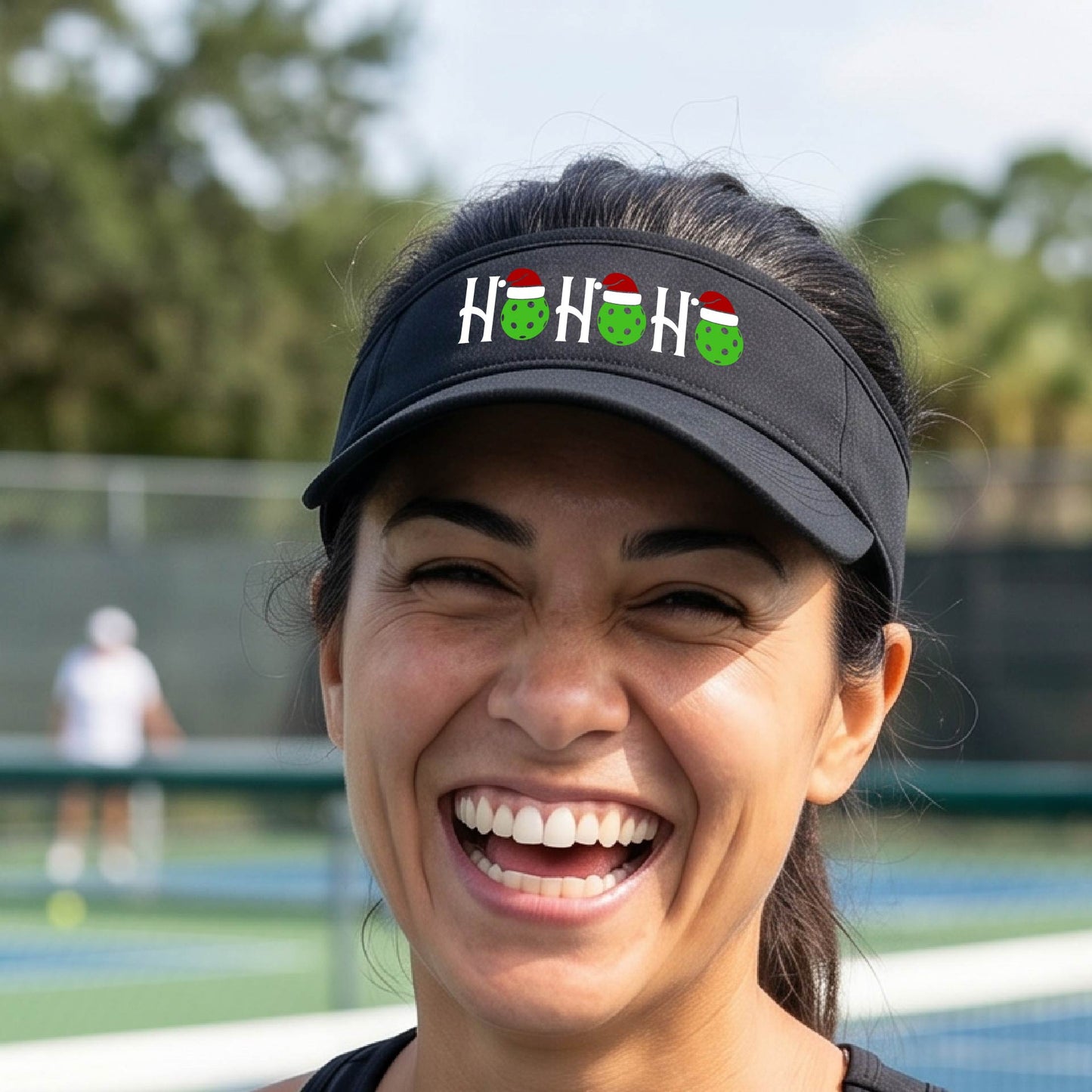 A navy blue visor with a pickleball Christmas graphic of the text "HO HO HO" with the O replaced by green picklebalsl paddle  santa hats. 
