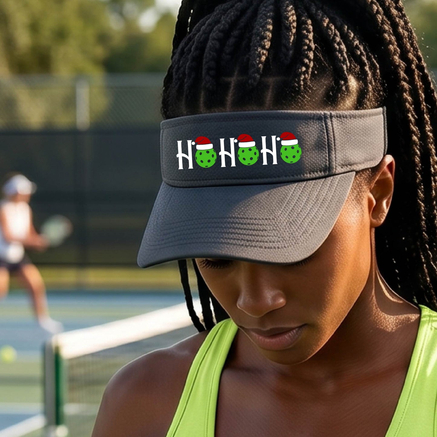A graphite gray visor with a pickleball Christmas graphic of the text "HO HO HO" with the O replaced by green picklebalsl paddle  santa hats. 