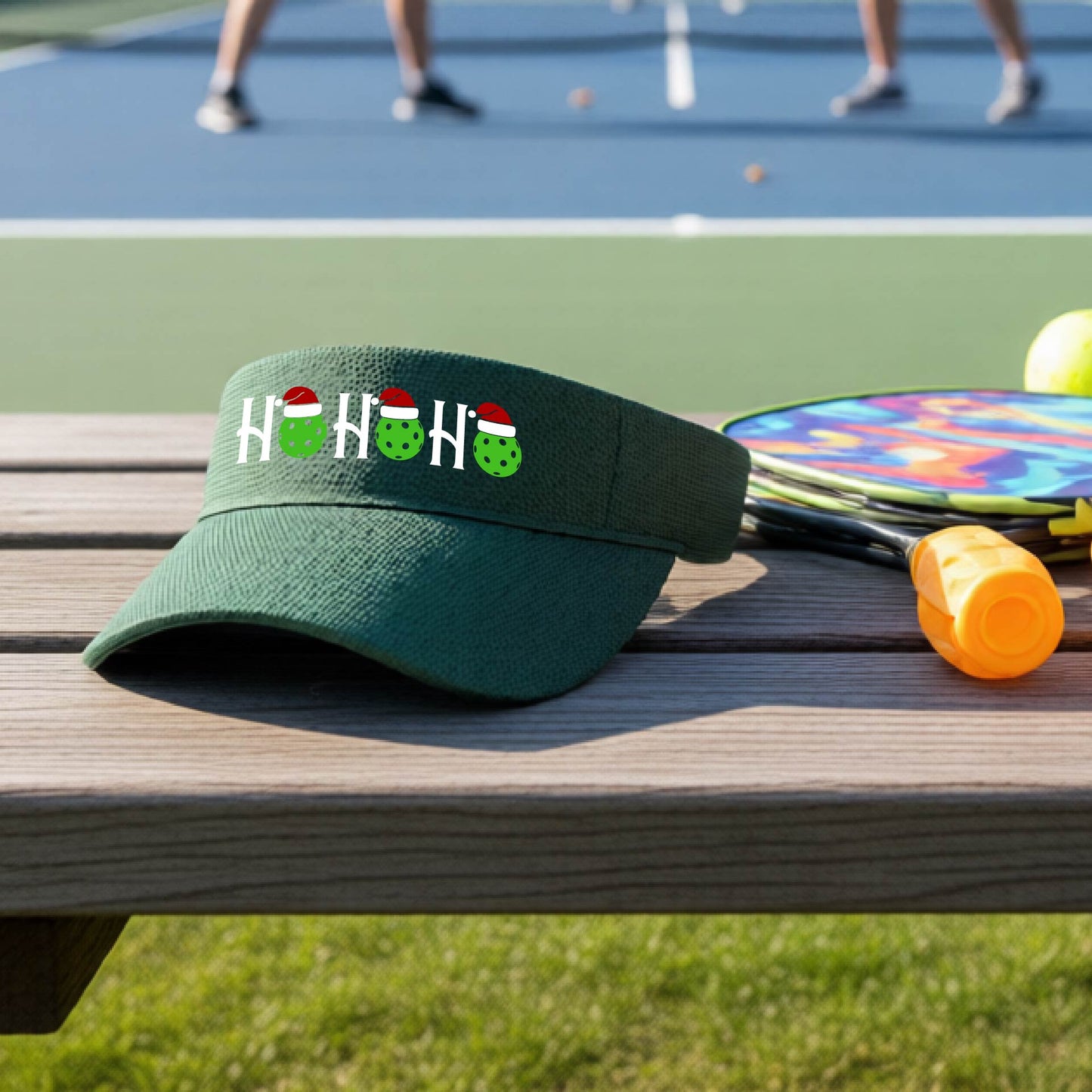 A green visor with a pickleball Christmas graphic of the text "HO HO HO" with the O replaced by green picklebalsl paddle  santa hats. 