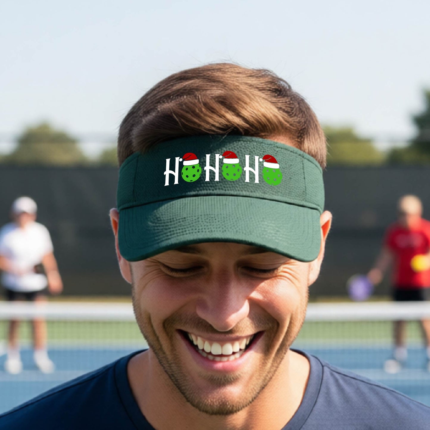 A green visor with a pickleball Christmas graphic of the text "HO HO HO" with the O replaced by green picklebalsl paddle  santa hats. 