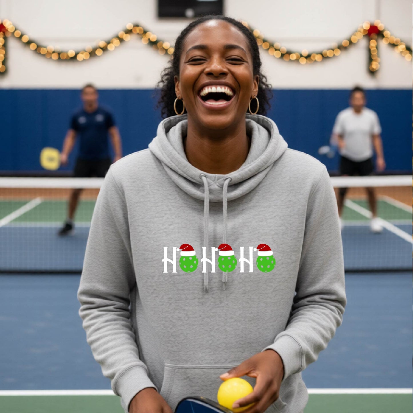 A gray cowl-neck hooded sweatshirt featuring a graphic print that reads "Ho Ho Ho'" in white text. The design includes pickleball replacing the O in the text.