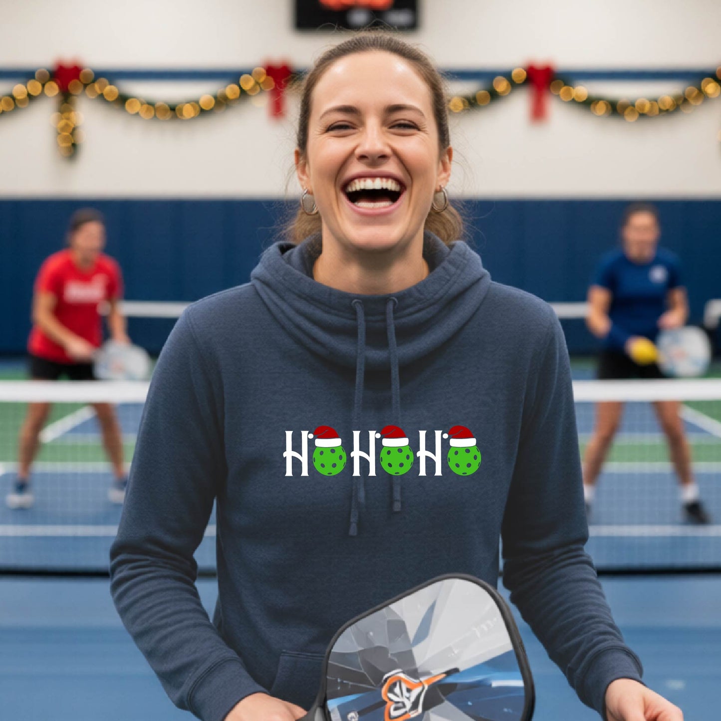 A navy blue cowl-neck hooded sweatshirt featuring a graphic print that reads "Ho Ho Ho'" in white text. The design includes pickleball replacing the O in the text.