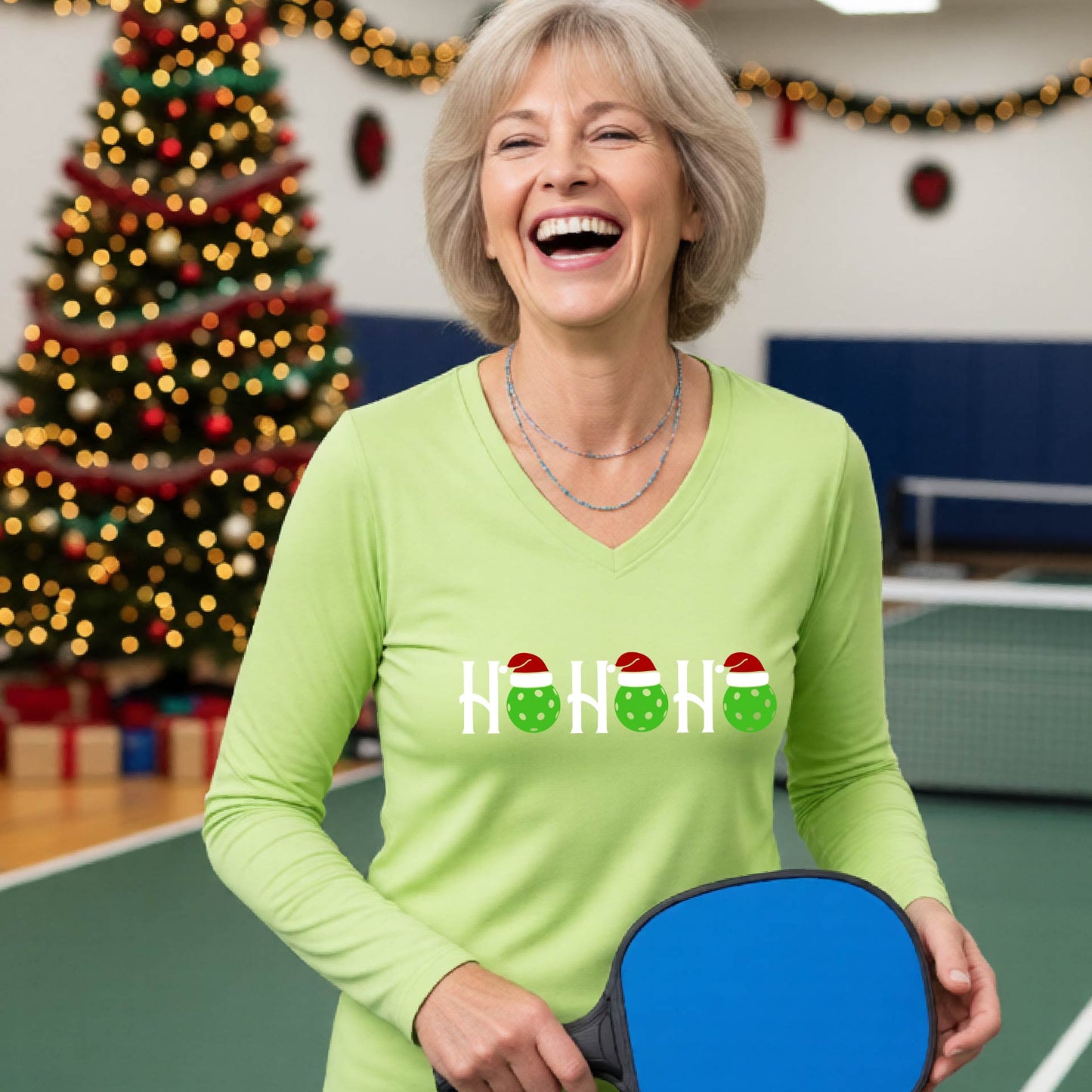 A women's lime green long-sleeve v-neck shirt featuring a pickleball graphic with text "HO HO HO"  with the O replaced by green pickleballs wearing a santa hats and  Christmas themed background.