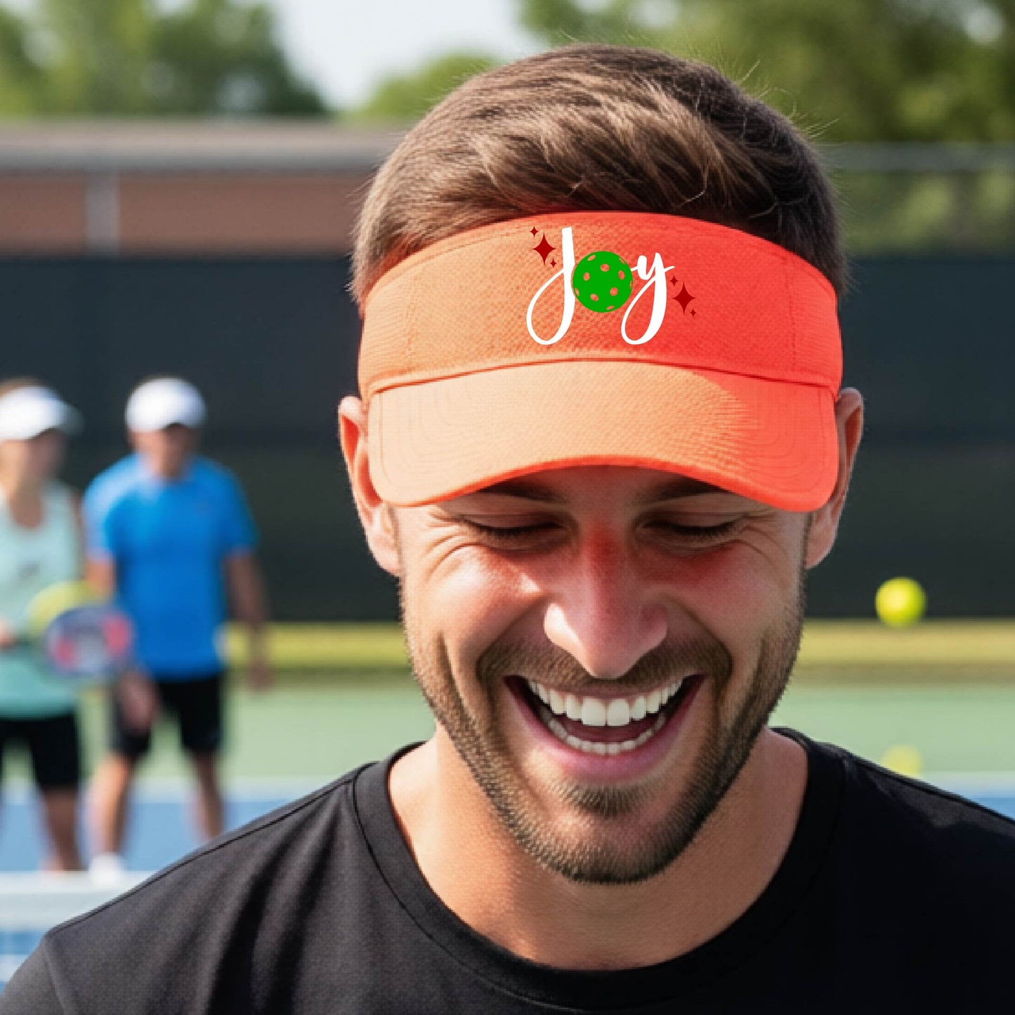 An orange visor with a pickleball Christmas graphic of the text "JOY" with the O replaced by a green pickleball. 