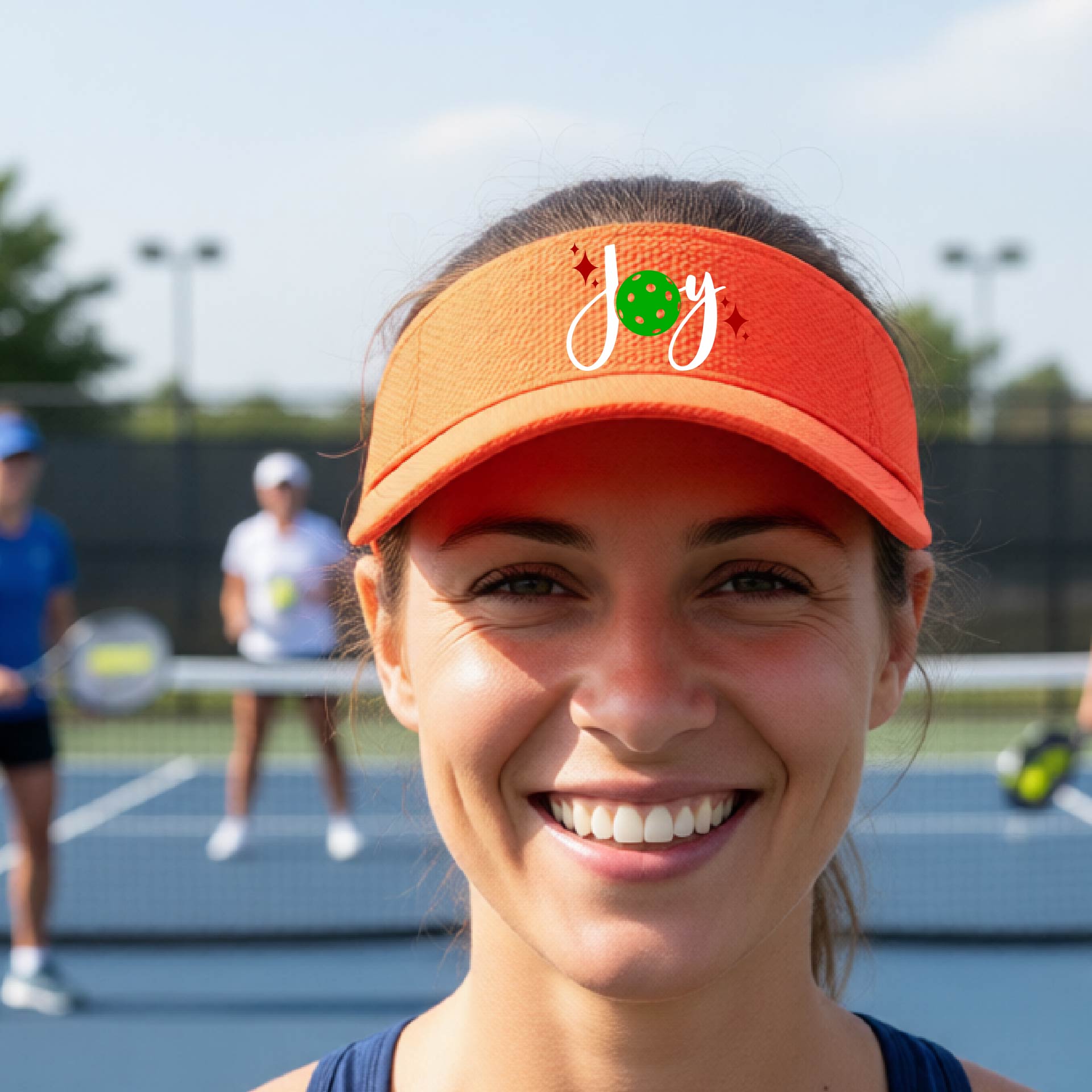 An orange visor with a pickleball Christmas graphic of the text "JOY" with the O replaced by a green pickleball. 