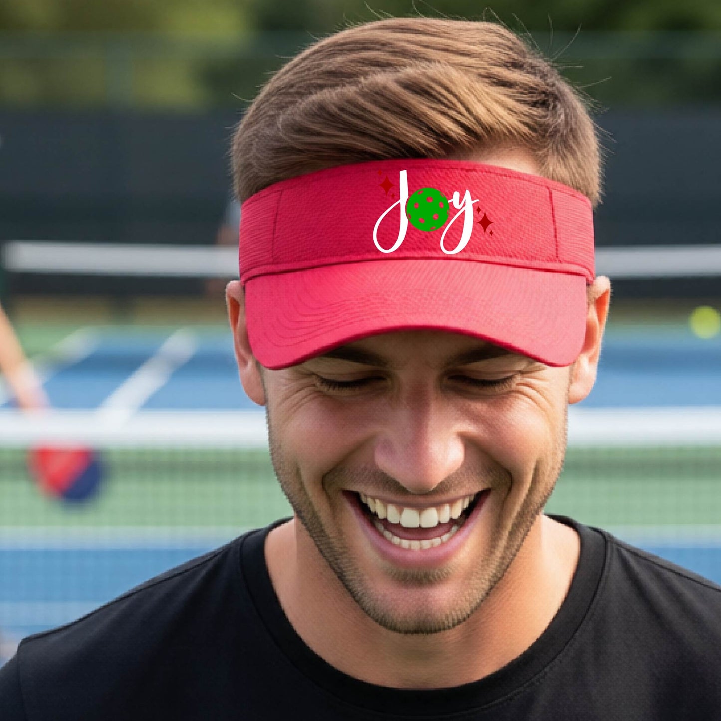 A red visor with a pickleball Christmas graphic of the text "JOY" with the O replaced by a green pickleball. 