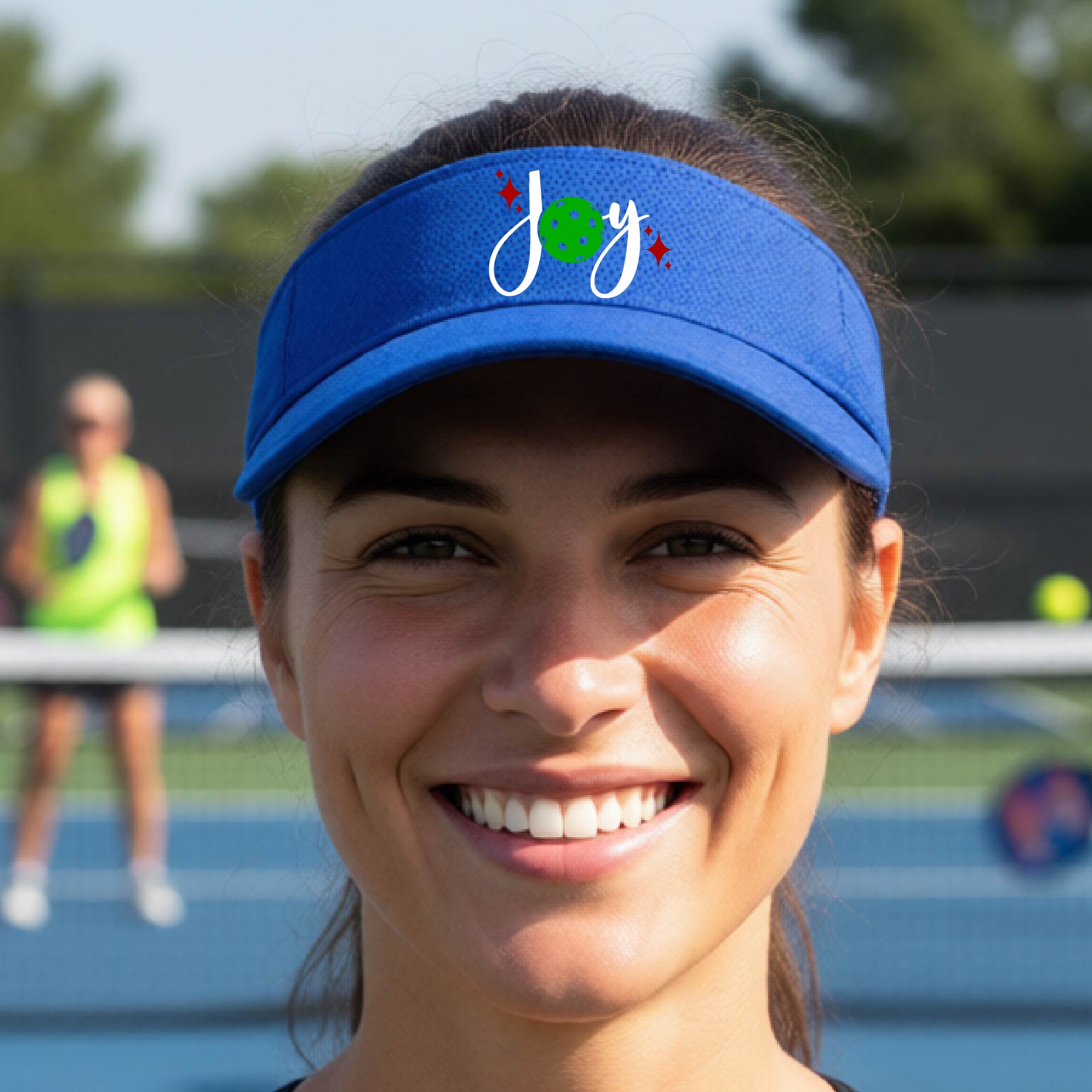 A royal blue visor with a pickleball Christmas graphic of the text "JOY" with the O replaced by a green pickleball. 