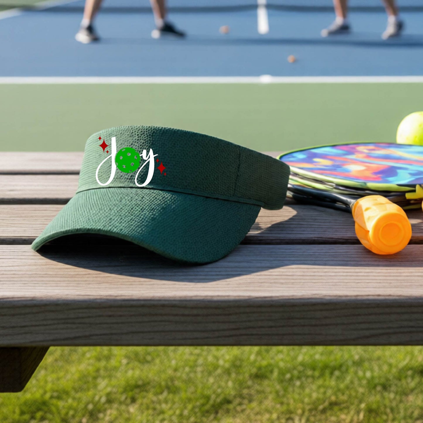 A green visor with a pickleball Christmas graphic of the text "JOY" with the O replaced by a green pickleball. 