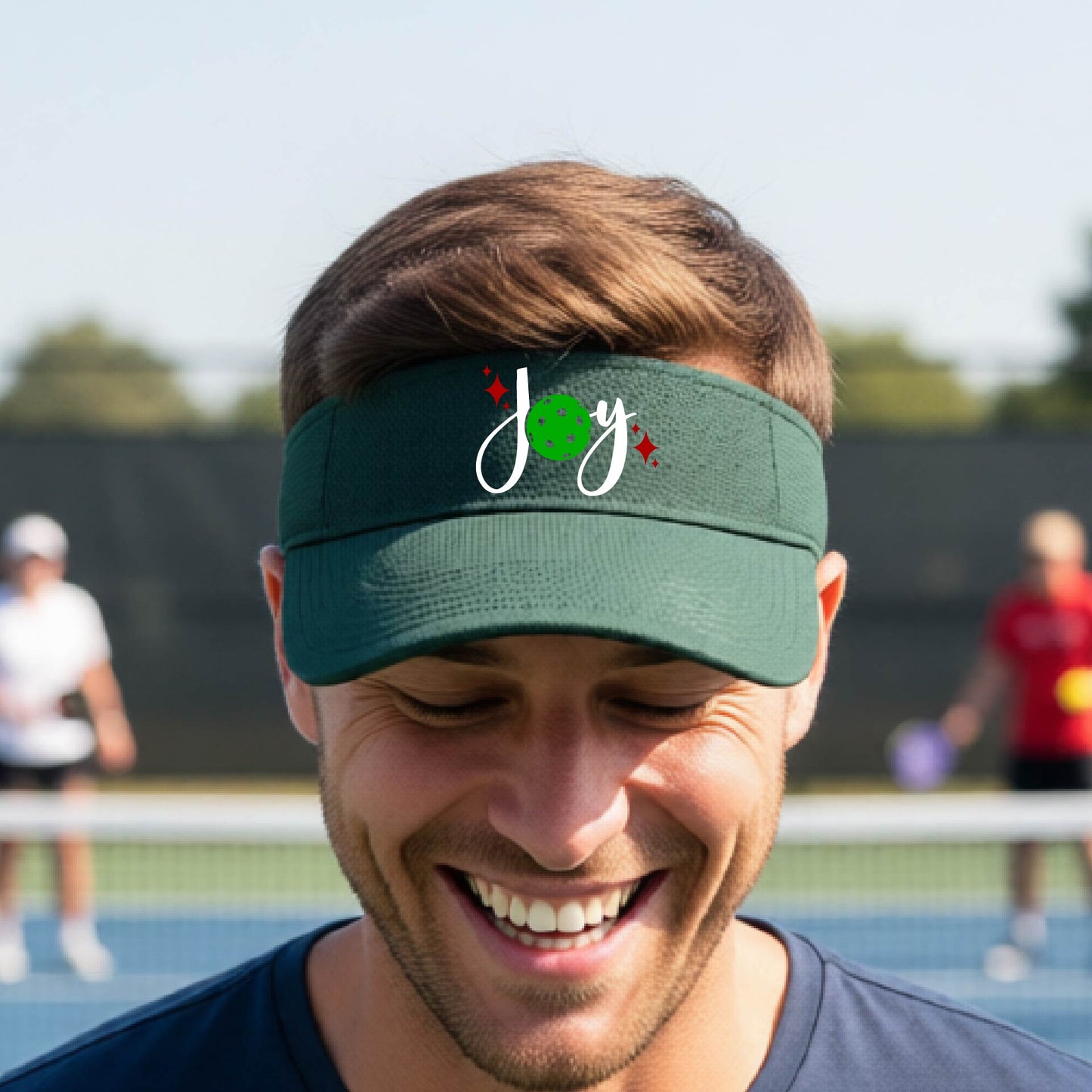A green visor with a pickleball Christmas graphic of the text "JOY" with the O replaced by a green pickleball. 