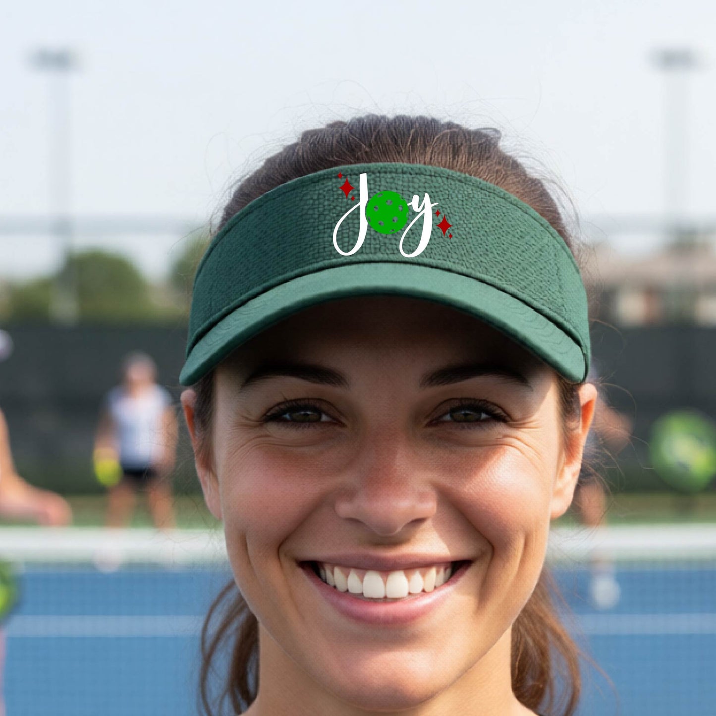 A green visor with a pickleball Christmas graphic of the text "JOY" with the O replaced by a green pickleball. 