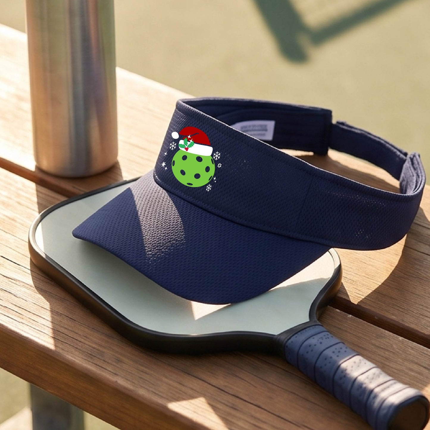 A navy blue visor with a pickleball Christmas graphic and green pickleball wearing a santa hat.