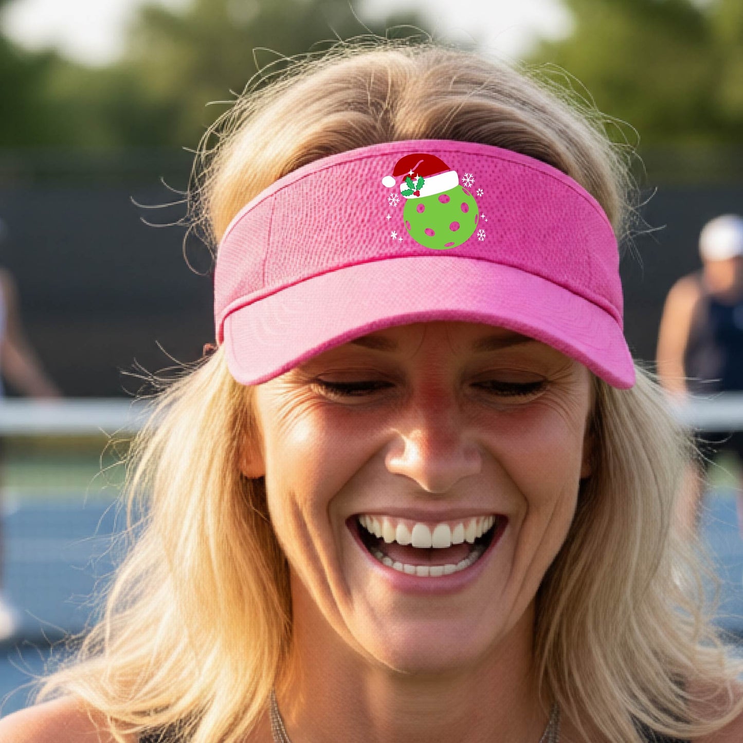 A pink visor with a pickleball Christmas graphic and green pickleball wearing a santa hat.