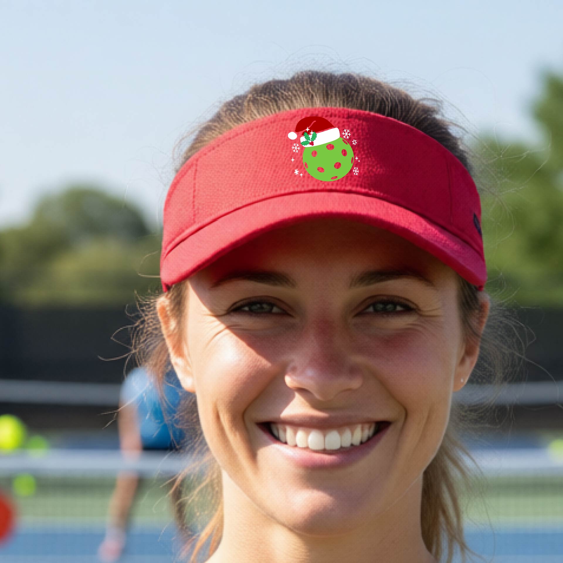 A red visor with a pickleball Christmas graphic and green pickleball wearing a santa hat.