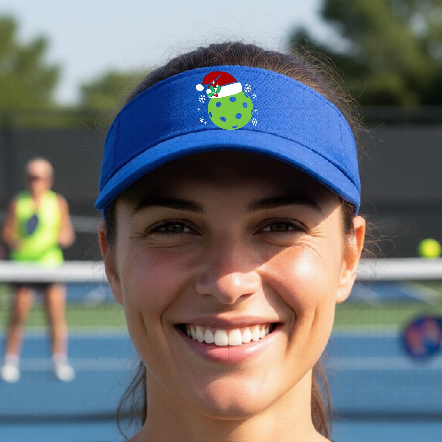 A royal blue visor with a pickleball Christmas graphic and green pickleball wearing a santa hat.