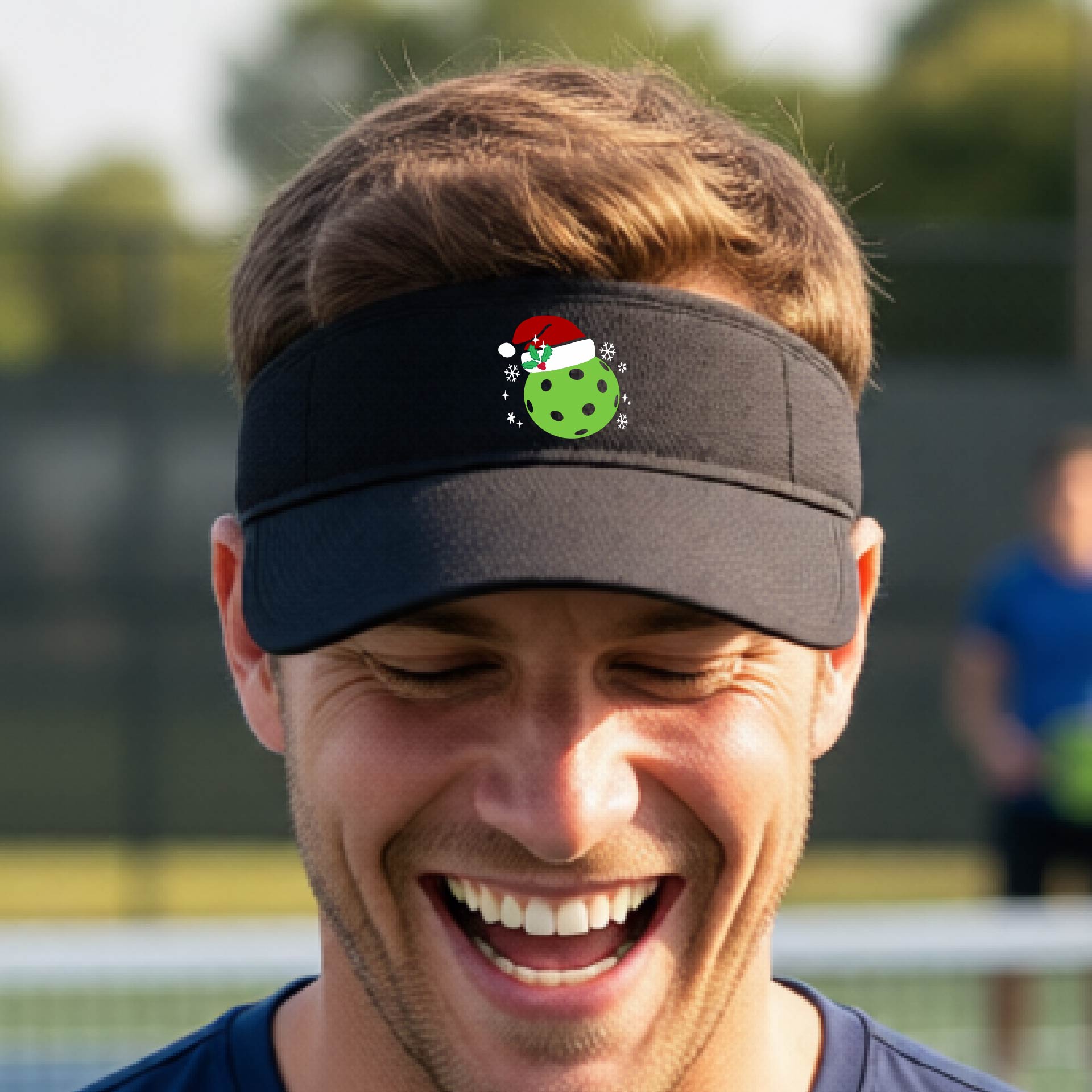 A black visor with a pickleball Christmas graphic and green pickleball wearing a santa hat.