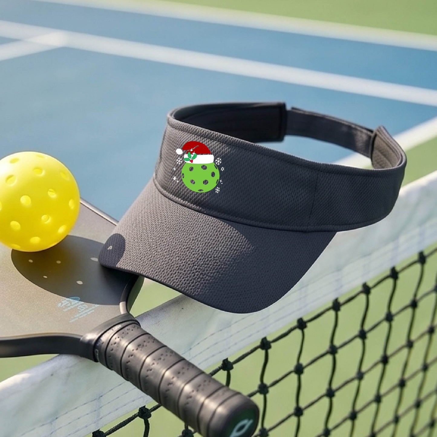 A graphite gray visor with a pickleball Christmas graphic and green pickleball wearing a santa hat.
