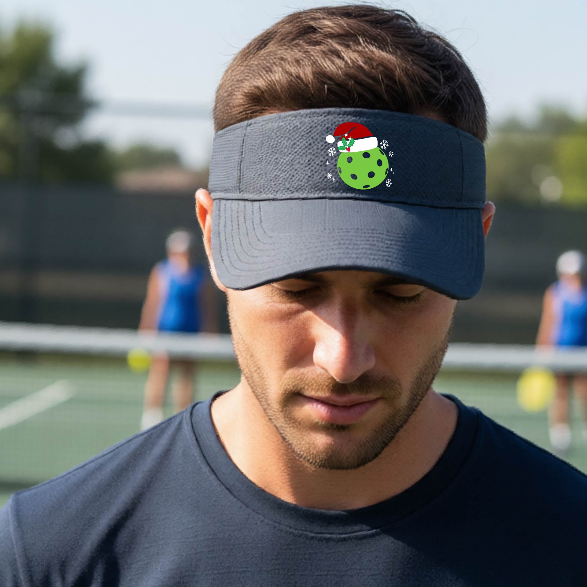 A graphite gray visor with a pickleball Christmas graphic and green pickleball wearing a santa hat.