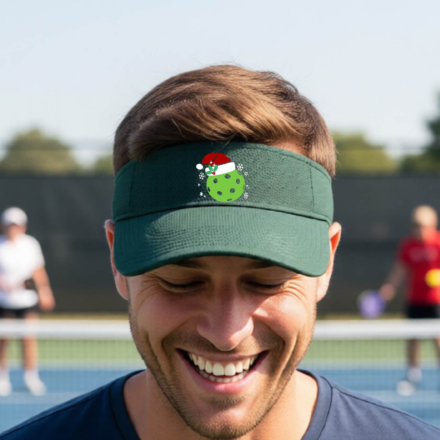 A green visor with a pickleball Christmas graphic and green pickleball wearing a santa hat.