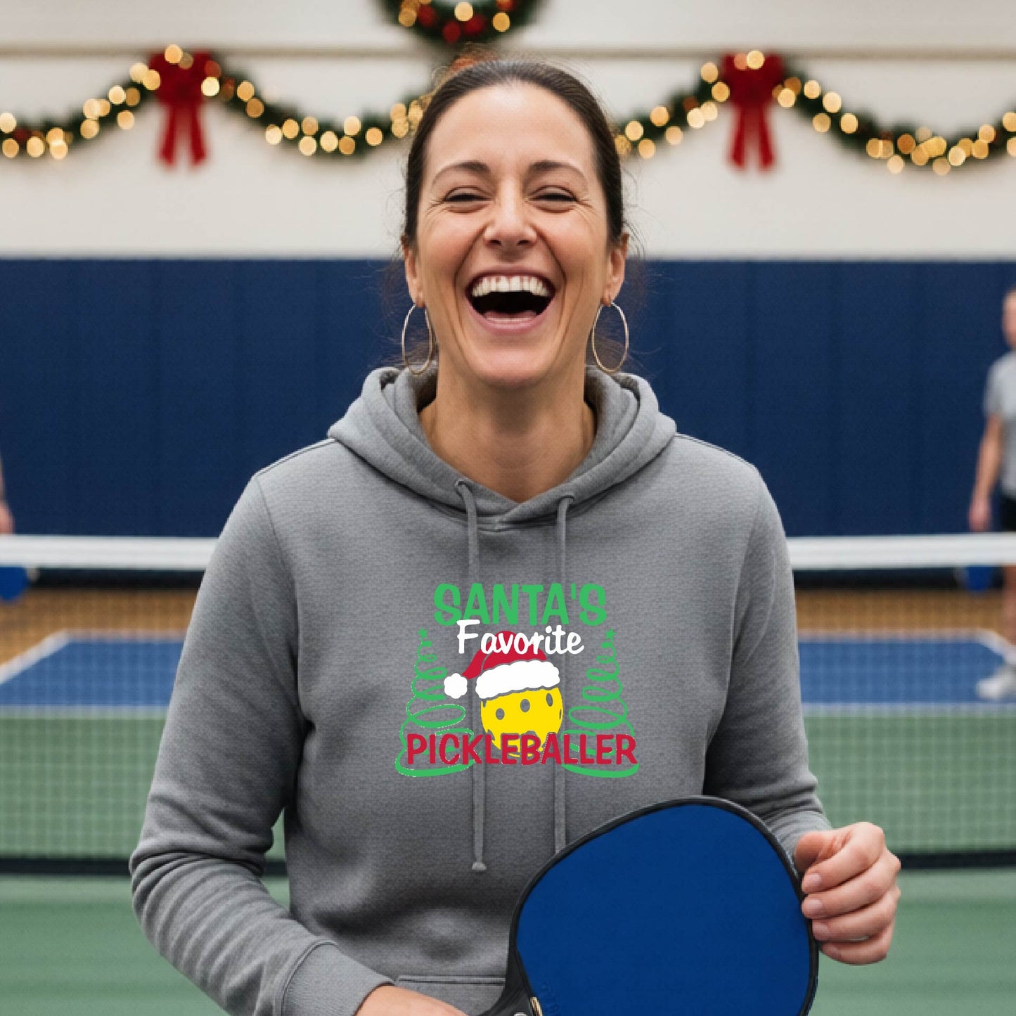 A gray hooded sweatshirt featuring a pickleball graphic with the text "SANTA'S FAVORITE PICKLEBALL." and a Christmas 