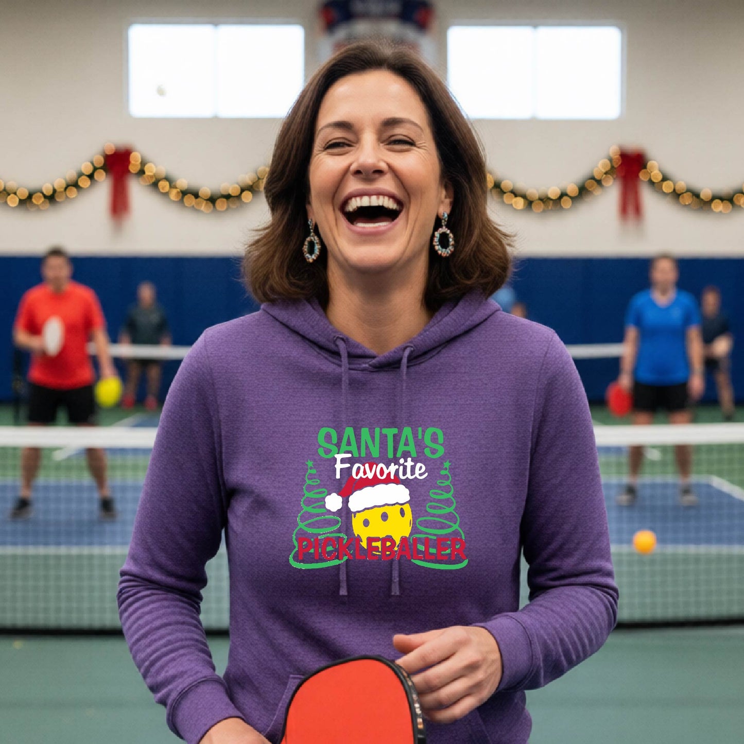A purple hooded sweatshirt featuring a pickleball graphic with the text "SANTA'S FAVORITE PICKLEBALL." and a Christmas 