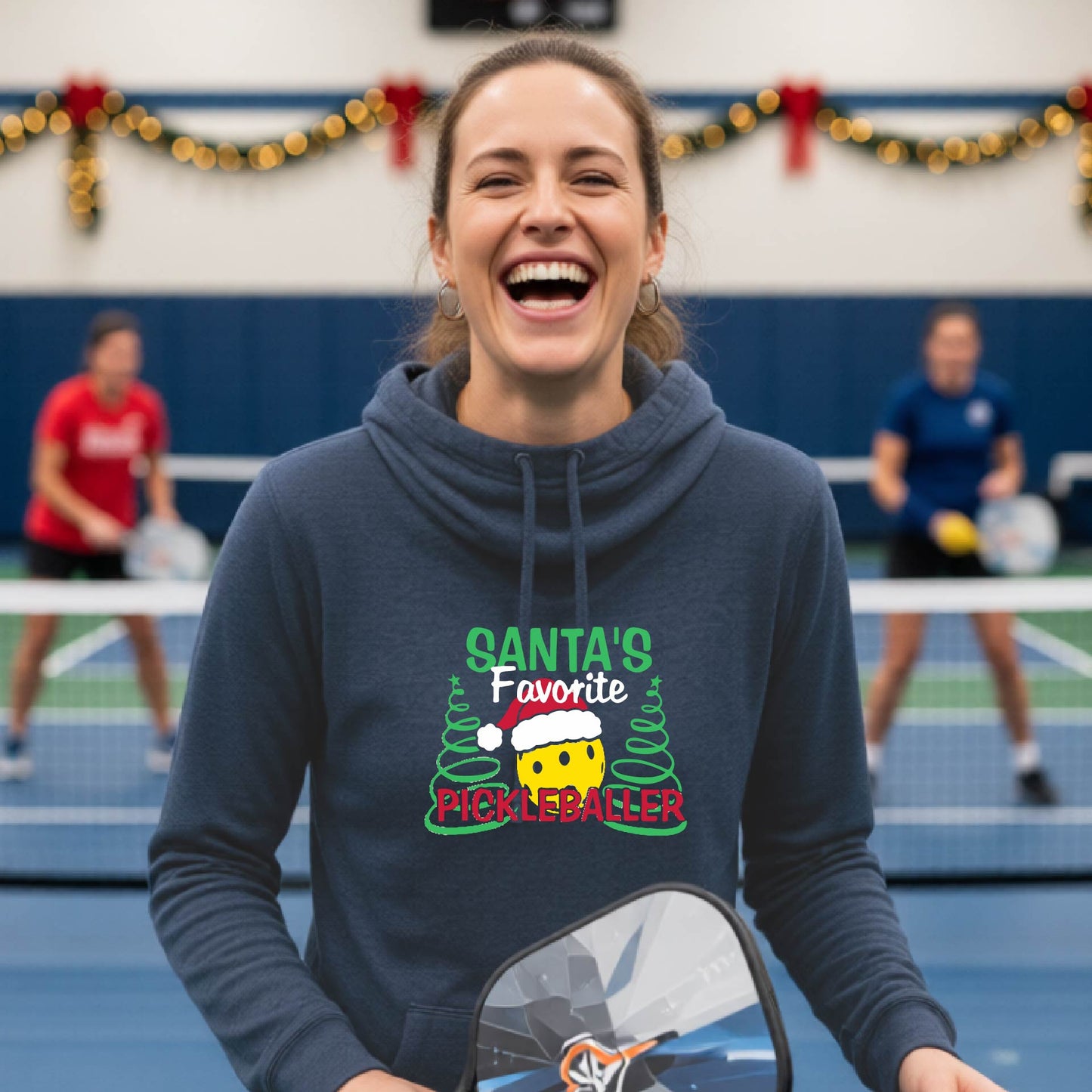 A navy blue cowl-neck hooded sweatshirt featuring a pickleball graphic and text "SANTA'S FAVORITE PICKLEBALLER" and Christmas themed background. 