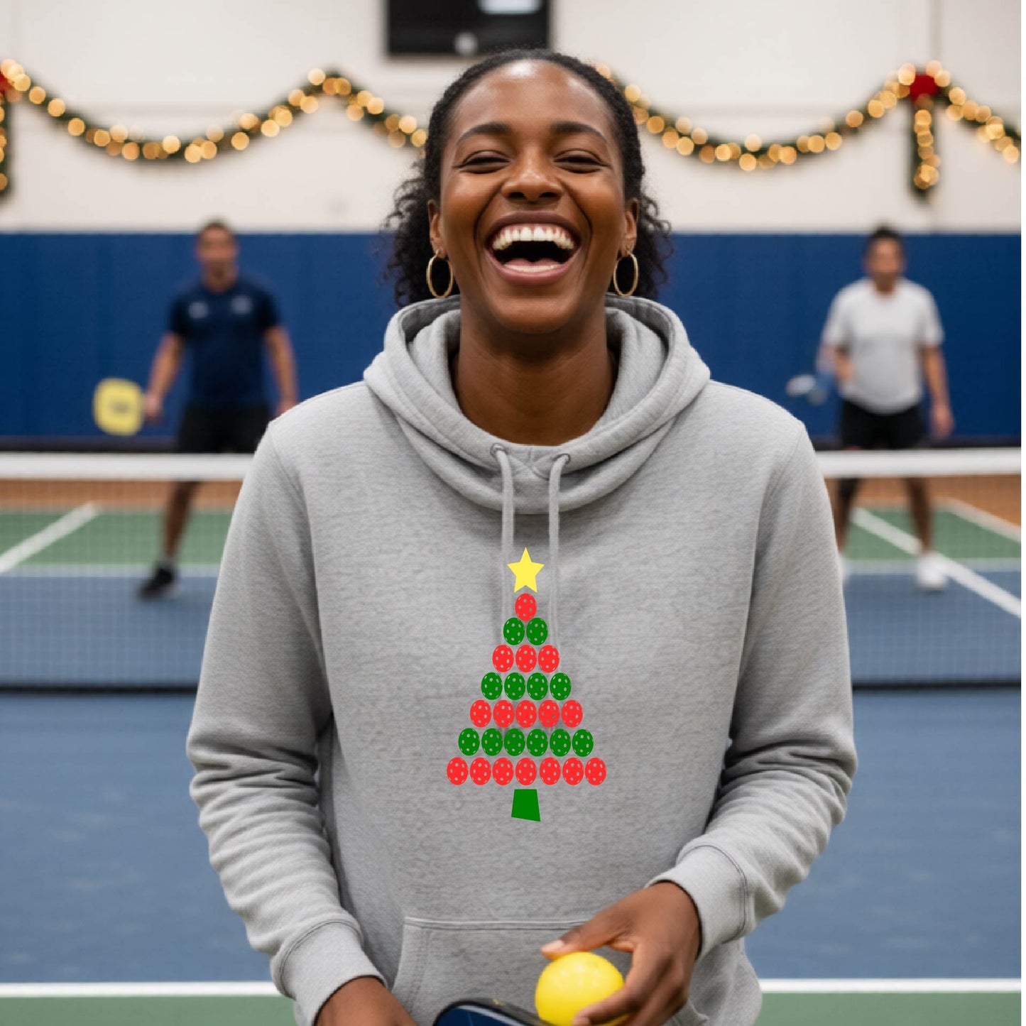 A gray blue cowl-neck hooded sweatshirt featuring a pickleball graphic of a tree made of pickleballs and a Christmas themed background. 