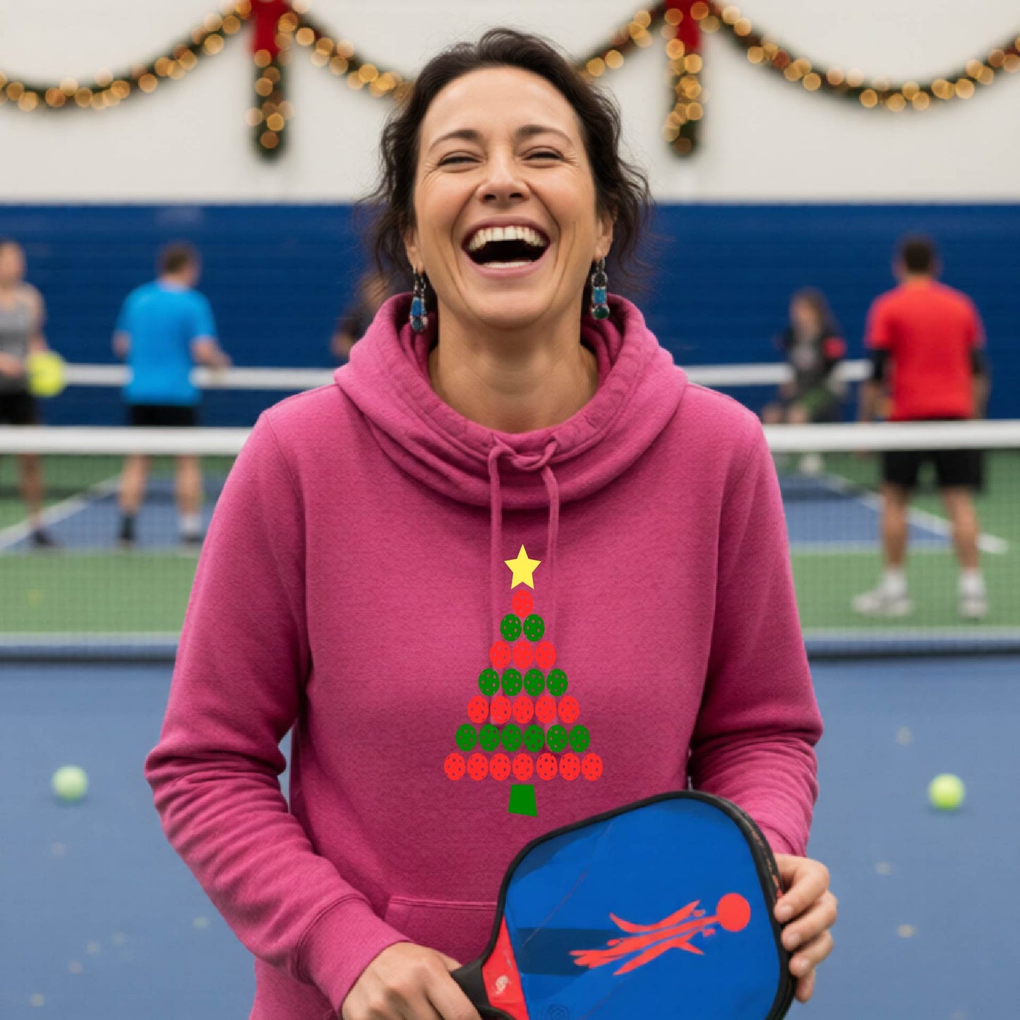 A pink cowl-neck hooded sweatshirt featuring a pickleball graphic of a tree made of pickleballs and a Christmas themed background. 