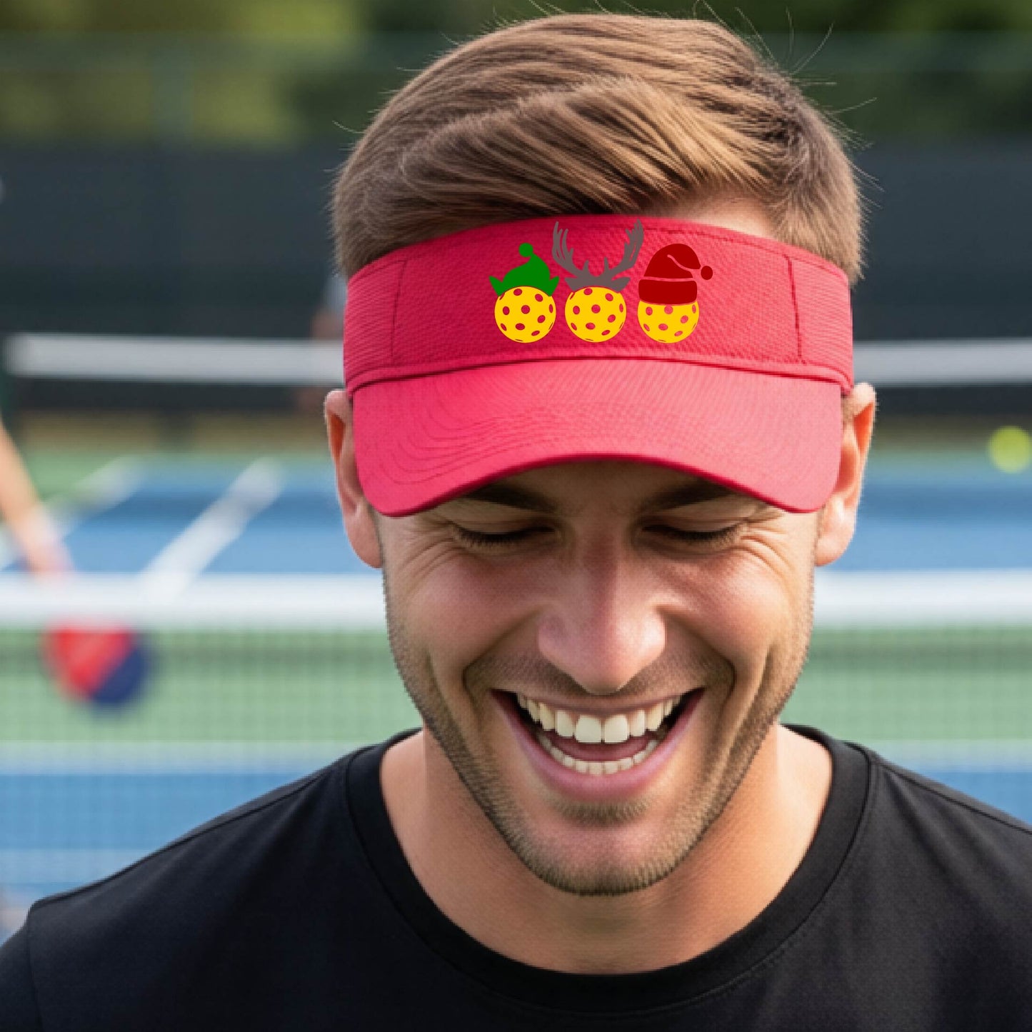 A red visor with a pickleball Christmas graphic of three pickleballs wearing a santa hat, elf hat and antlers. 