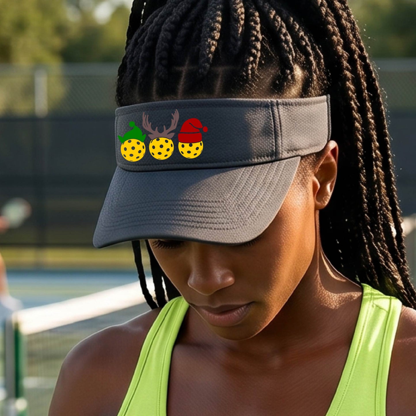 A graphite gray visor with a pickleball Christmas graphic of three pickleballs wearing a santa hat, elf hat and antlers. 