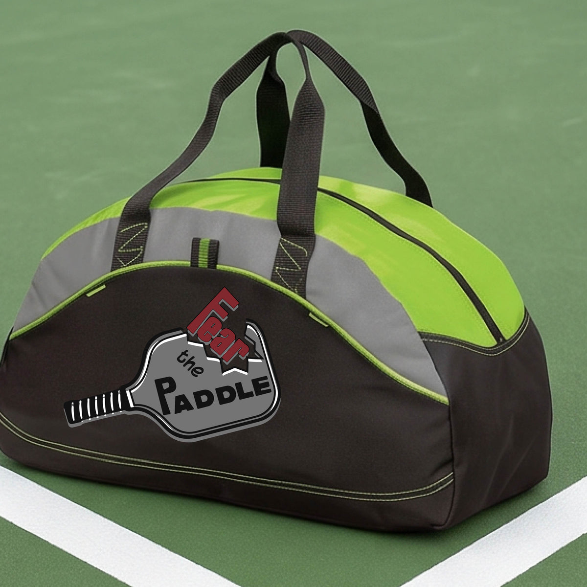 A lime green, gray and black duffel bag with a pickleball graphic of the text 'FEAR THE PADDLE' cut into a pickleball paddle, set on a background of a pickleball court. 