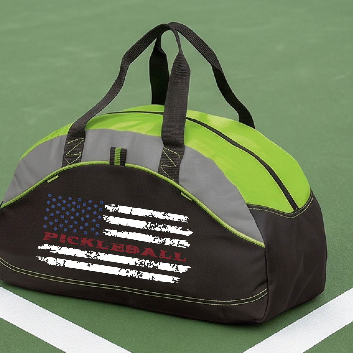 A lime green, black and gray duffel bag with a pickleball graphic of a distressed flag made out of pickleballs and the text 'PICKLEBALL' replacing one of the stripes, standing on a pickleball court.