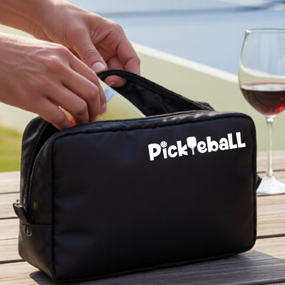 A black cosmetic toiletry bag with a white graphic of the word 'Pickleball' and an intergrated pickleball paddle replacing the L. 
