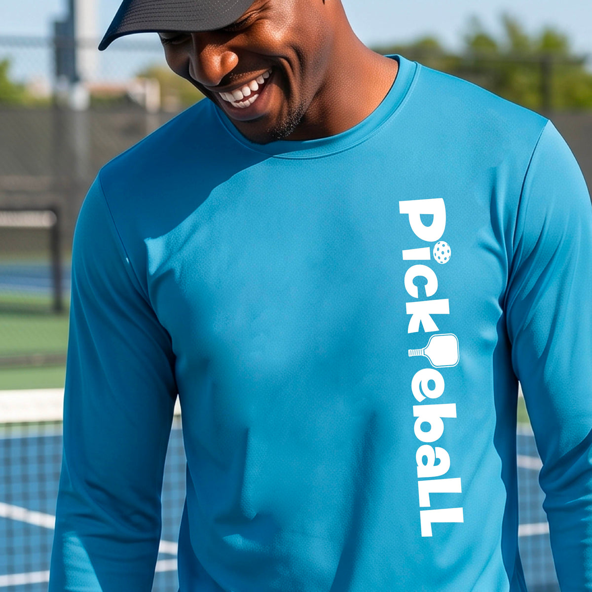 A man wearing a bright blue long-sleeve athletic shirt with 'Pickleball' printed vertically in white on the right side, standing on a pickleball court.