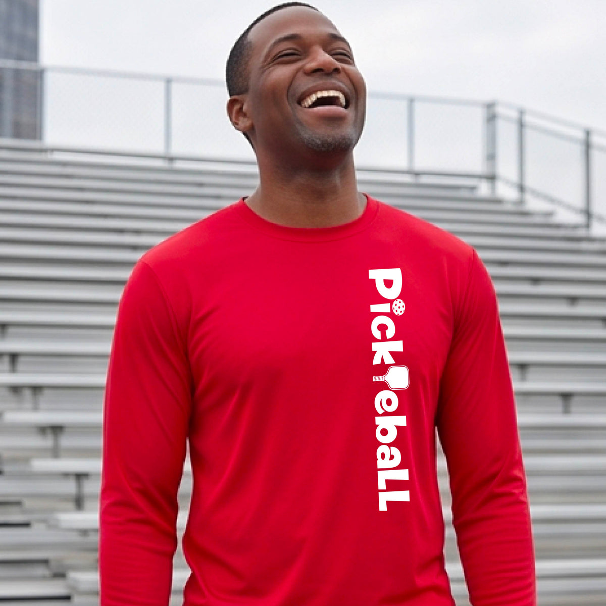 A man wearing a red long-sleeve athletic shirt with 'Pickleball' printed vertically in white on the right side of the chest.