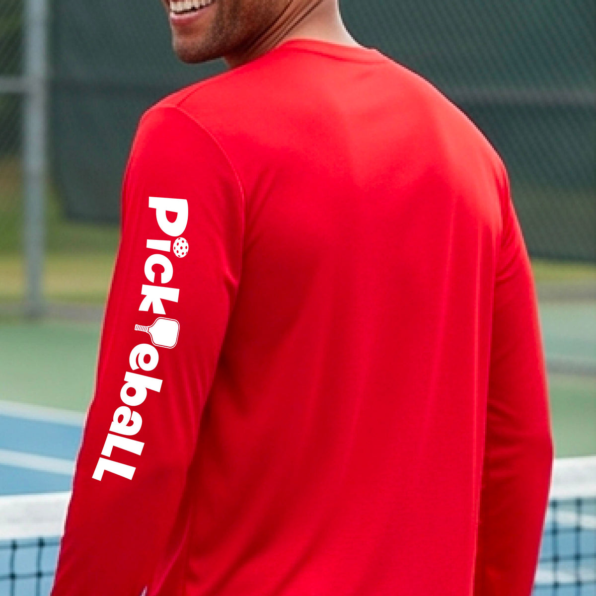 A man wearing a bright red long-sleeve athletic shirt, shown from the back and side. The shirt features the word 'Pickleball' printed vertically in white on the left sleeve, with a pickleball paddle graphic replacing the letter 'i'.